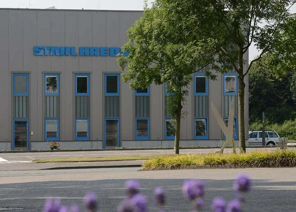 Company façade with lettering ‘STAHL KREBS’ Facade with STAHL KREBS lettering, blue window frames; trees in front, parked vehicle on the right.
