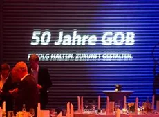 Die GOB feiert ihr fünfzigjähriges Jubiläum Schriftzug 50 Jahre GOB projiziert in weiß auf blauer Leinwand vor festlich gedecktem Tisch