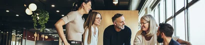 Zusammenarbeit und Prozesse in Vereinen und Verbänden effizient organisieren – mit unitop Symbolbild: Fünf Personen stehen zusammen und lachen in einem hellen Büro mit großen Fenstern.