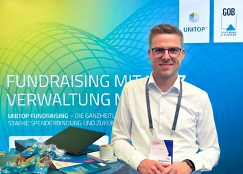 Tim Wagemans am GOB-Stand beim DFK 2025 mit Infomaterial, Give-aways und Kaffee im Vordergrund