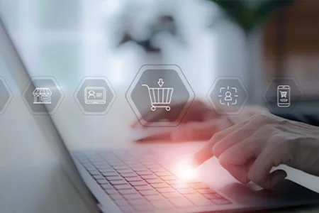 Hands typing on a laptop, icons for shopping cart, customers, channels – multichannel e-commerce.