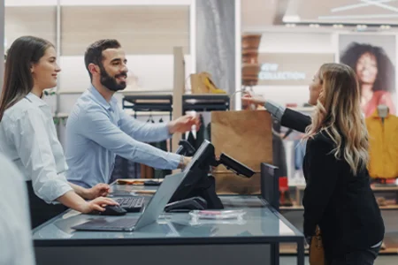 Sales assistant hands shopping bag to customer in modern fashion store.