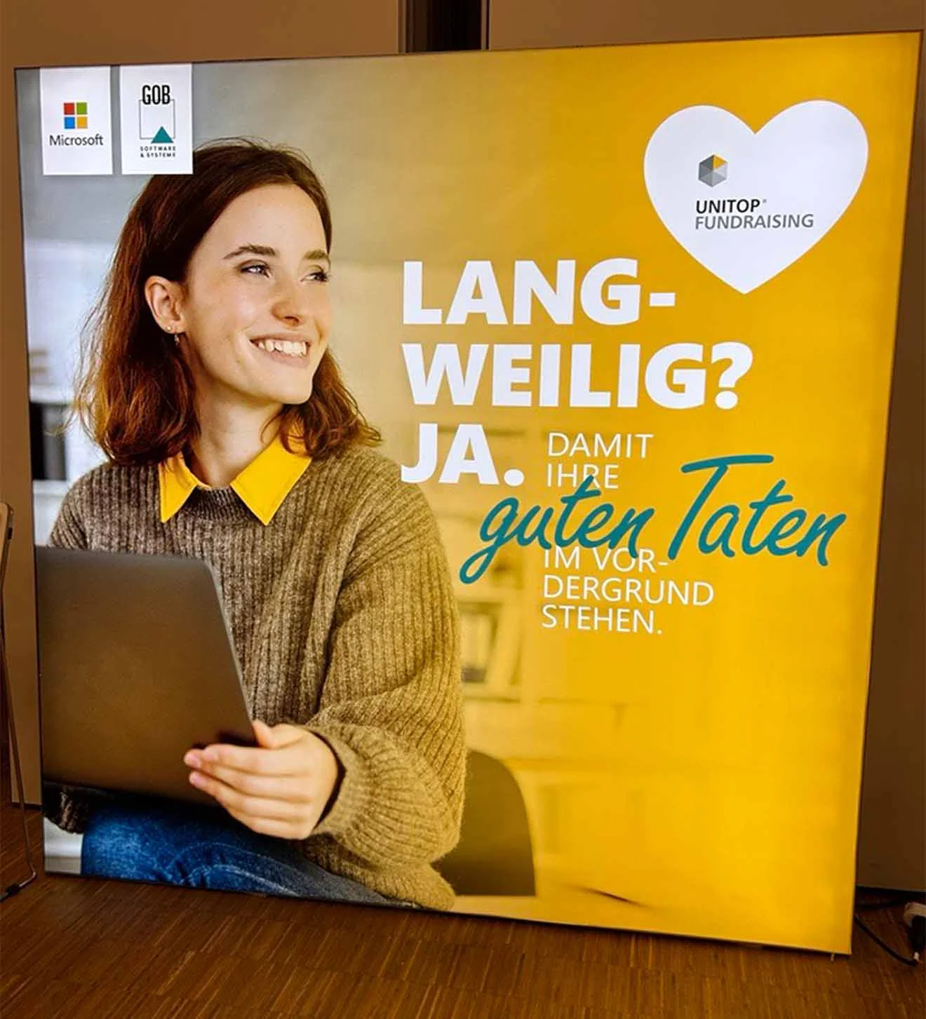Plakat auf GOB-Stand auf dem DFK 2024 Plakat auf GOB-Stand, Frau am Laptop, gelber Hintergrund, unitop-Fundraising-Logo