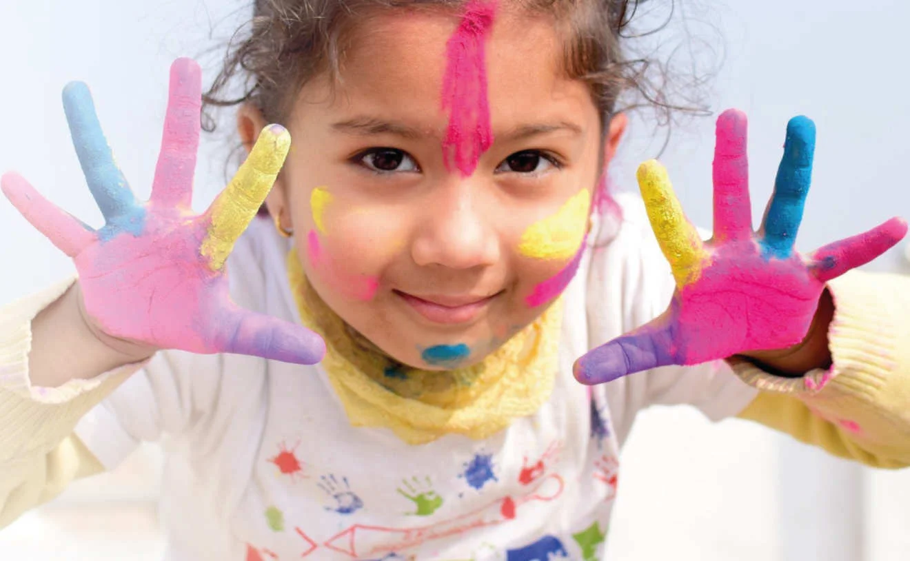 Kind mit bunten Farben im Gesicht – Aktion der Deutschen Kinderkrebsstiftung Kind mit bunter Farbe auf Händen und im Gesicht lächelt bei der Deutschen Kinderkrebsstiftung.