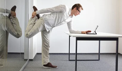 Gesundheit am Arbeitsplatz: Mit kleinen Übungen fit bleiben Gesundheit am Arbeitsplatz: Mann macht Dehnübung am Schreibtisch, Laptop daneben