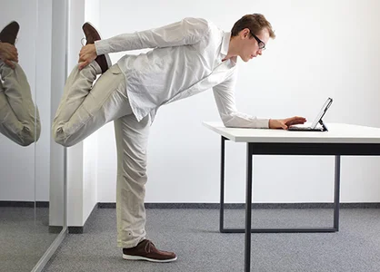 Gesundheit am Arbeitsplatz: Mit kleinen Übungen fit bleiben Gesundheit am Arbeitsplatz: Mann macht Dehnübung am Schreibtisch, Laptop daneben