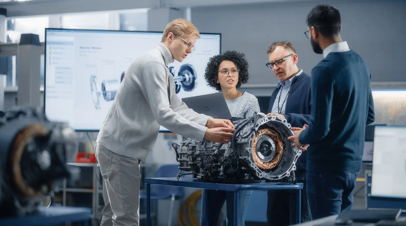 Ingenieurteam begutachtet Motorkomponenten und diskutiert technische Details vor einem Bildschirm.