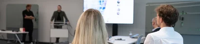 Bestens ausgestattet für den Start bei der GOB Neue GOB-Trainees sitzen im Schulungsraum und hören bei der IT-Geräte-Ausgabe zu.