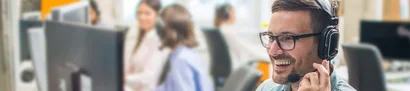 The GOB service team helps in case of faults Smiling male customer service representative wearing a headset, assisting clients in a busy office.