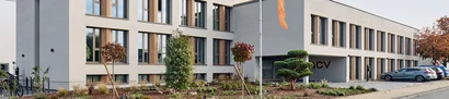 Der ACV-Hauptsitz in Köln ACV-Hauptsitz in Köln, mit moderner Fassadengestaltung, bepflanztem Vorbereich und Parkplatz.