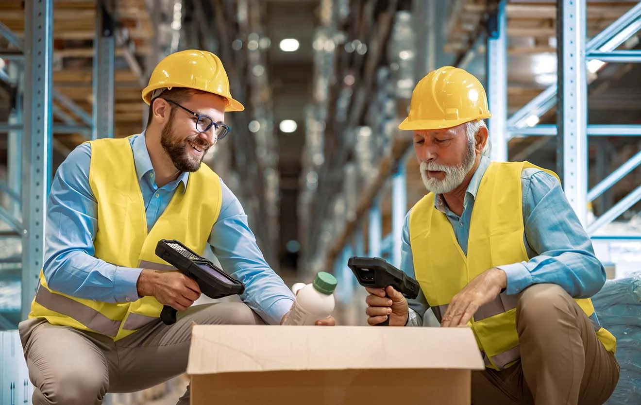 Mobile Datenerfassung im Großhandel bei Wareneingang – digital im ERP erfasst Zwei Lagerarbeiter im Großhandel scannen Produkte aus einem Karton mit Handscannern.