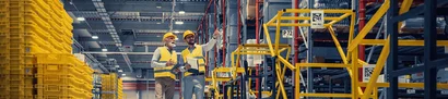 Großhandel: effiziente Logistik im Hochregallager Großlager mit gelben Kisten, hohen Regalen und zwei Mitarbeitenden in Warnwesten im Gang.