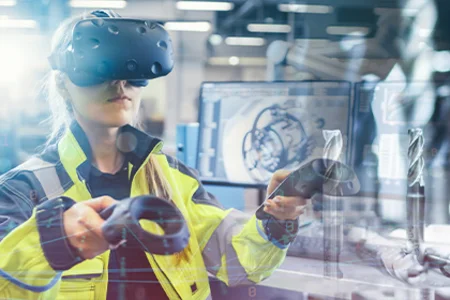 Symbolbild: Person mit VR-Brille und Controllern in der Fertigung, im Hintergrund Maschinen.