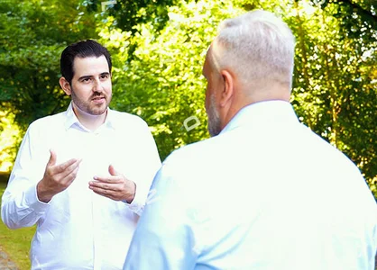 Zwei Männer im Gespräch bei „Walk and Talk“-Format im Grünen, rechte Bildhälfte mit Porträtaufnahme