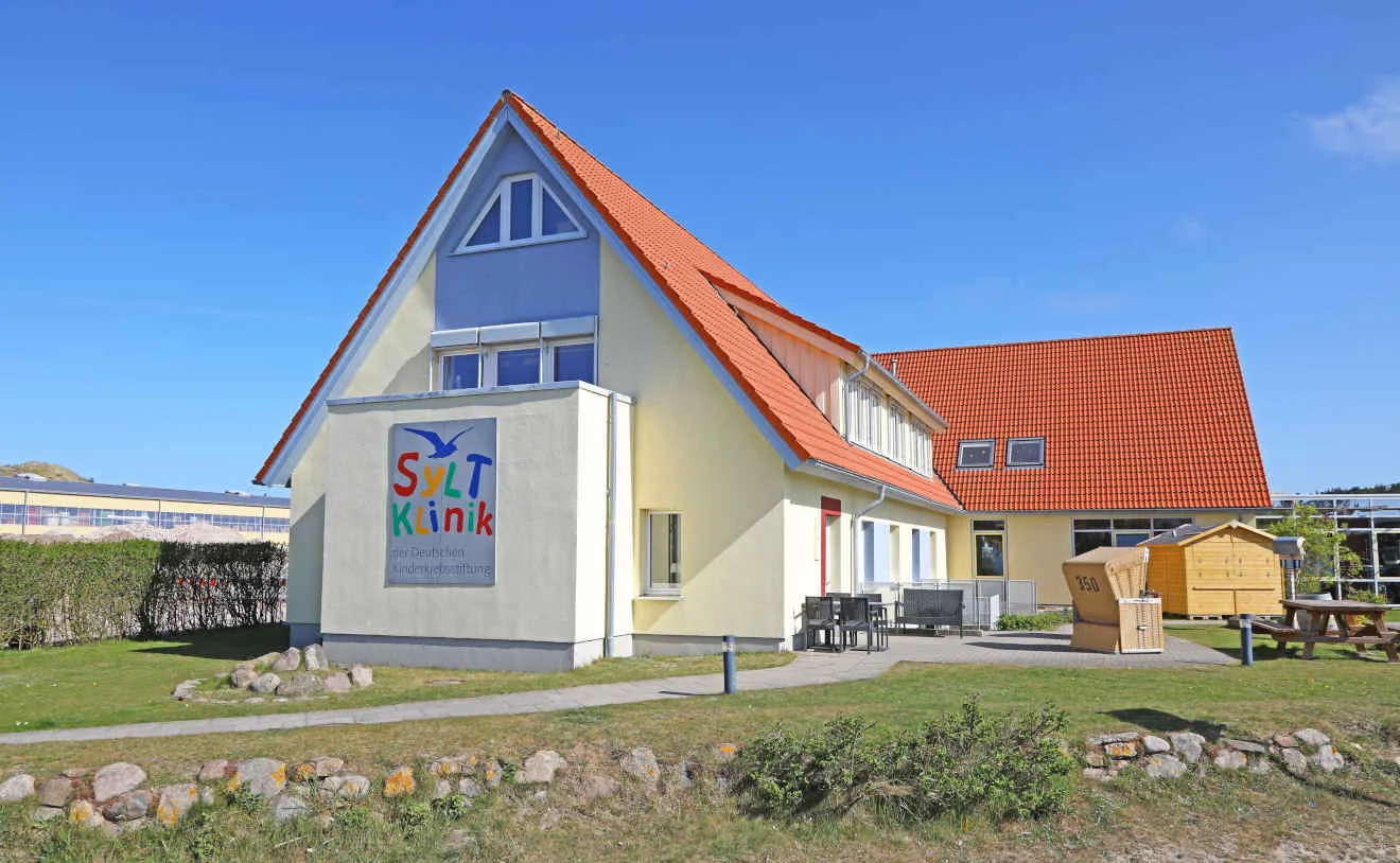 Gesamtansicht der SyltKlinik der Deutschen Kinderkrebsstiftung auf Sylt Gesamtansicht der gelben SyltKlinik der Deutschen Kinderkrebsstiftung mit Garten und rotem Dach.